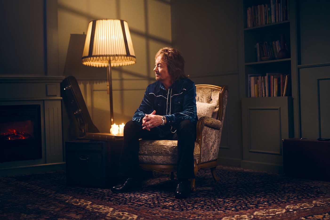 Chris Norman sits on an antique chair next to a fireplace.